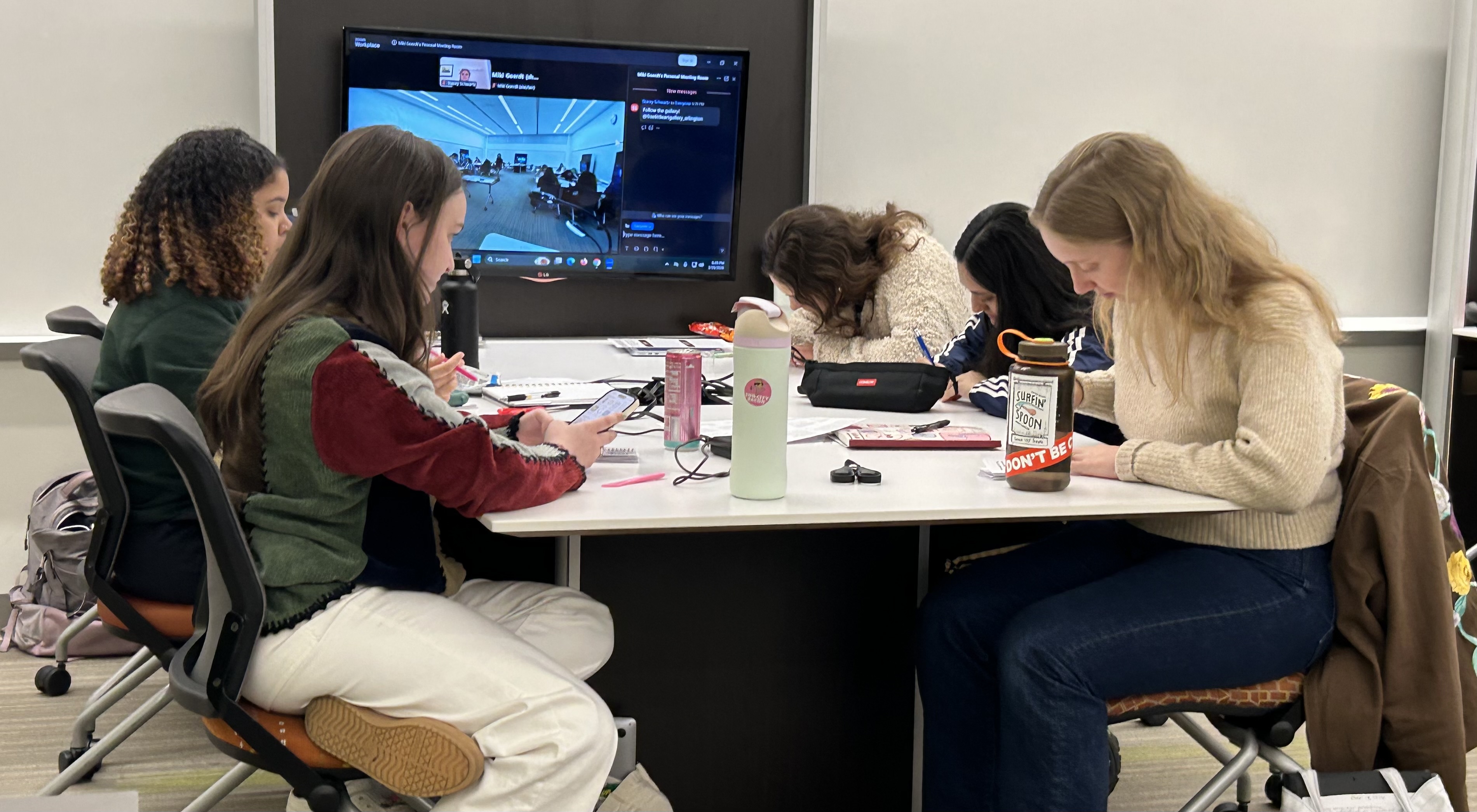 5 students sitting around a white table and drawing their designs for their mini prints for the Free Little Art Gallery.